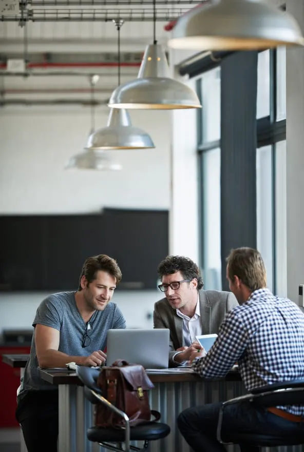 Three colleagues reviewing work together around a laptop